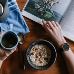Top view of a person having a healthy breakfast with cereal and tea while reading a magazine, illustrating a calm and productive morning routine.