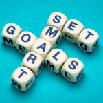 Lettered dice spelling out 'SMART' and 'GOALS' in a crossword format on a turquoise background, representing the concept of setting SMART goals.