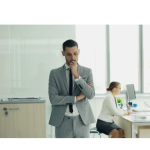 Thoughtful business leader reflecting on team communication challenges in a modern office environment, with colleagues working in the background, representing workplace communication, leadership, and team dynamics