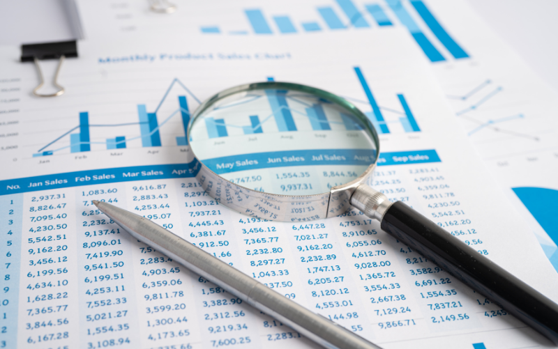 Magnifying glass focusing on financial data charts and Excel tables with a pen, representing data analysis, business reporting, and advanced Excel skills