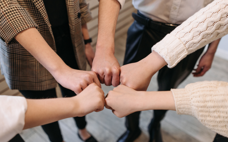 Team members joining fists in a circle, symbolising trust, collaboration and strong workplace communication.